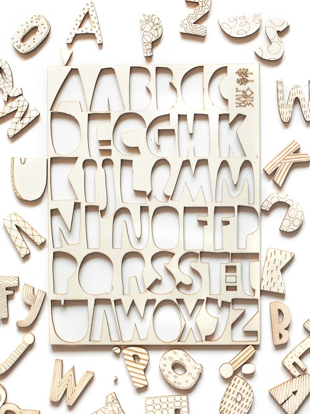 neben einem ausgestanzten Holztableau liegen viele Holzbuchstaben mit gelaserten Mustern