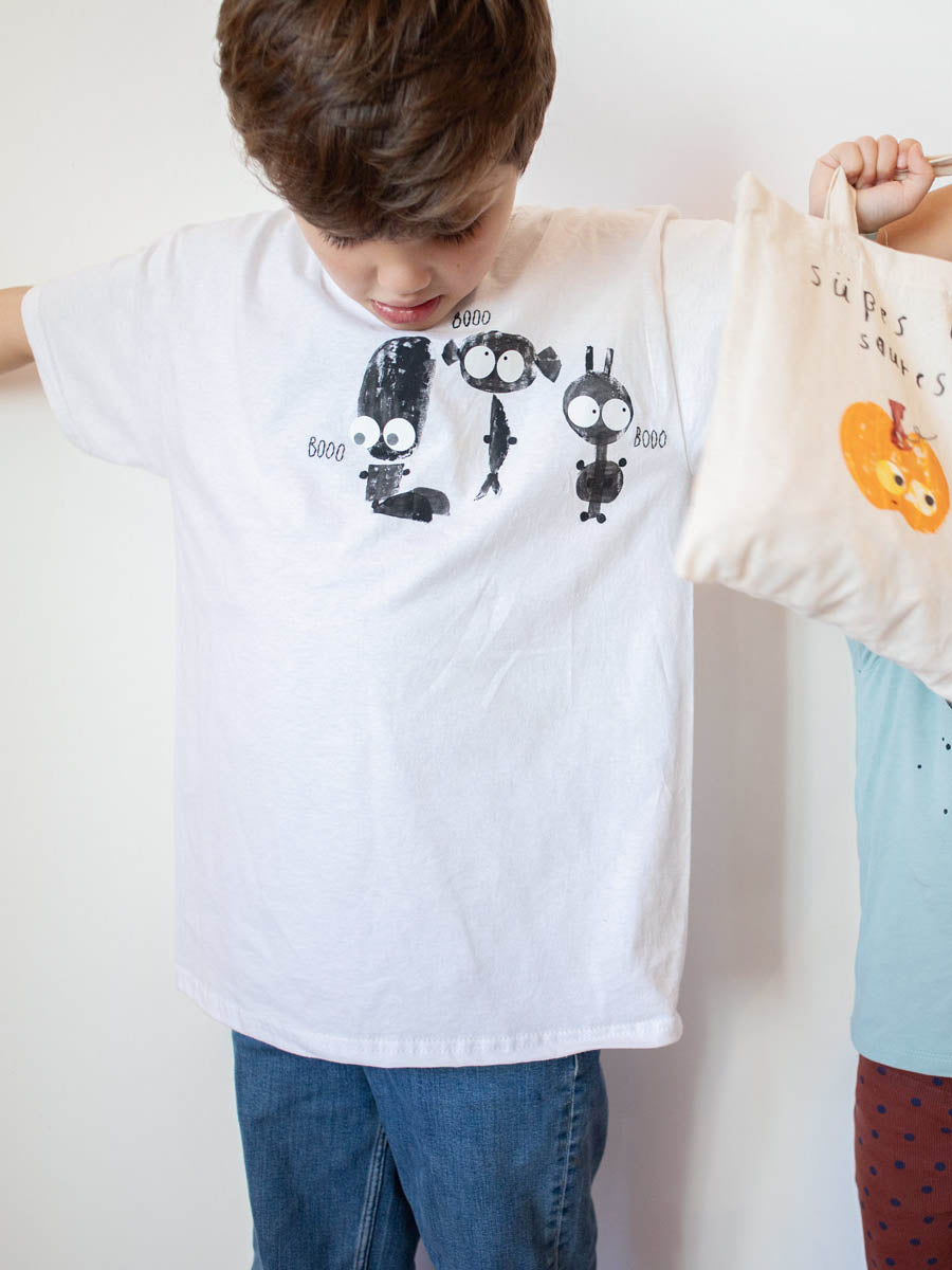 Kind trägt ein selbstgemachtes shirt in weiß mit kartoffeldruck und bügelbilder augen von halfbirdmona, daneben hängt eine Tasche mit süses oder saures und einem kürbis und augen