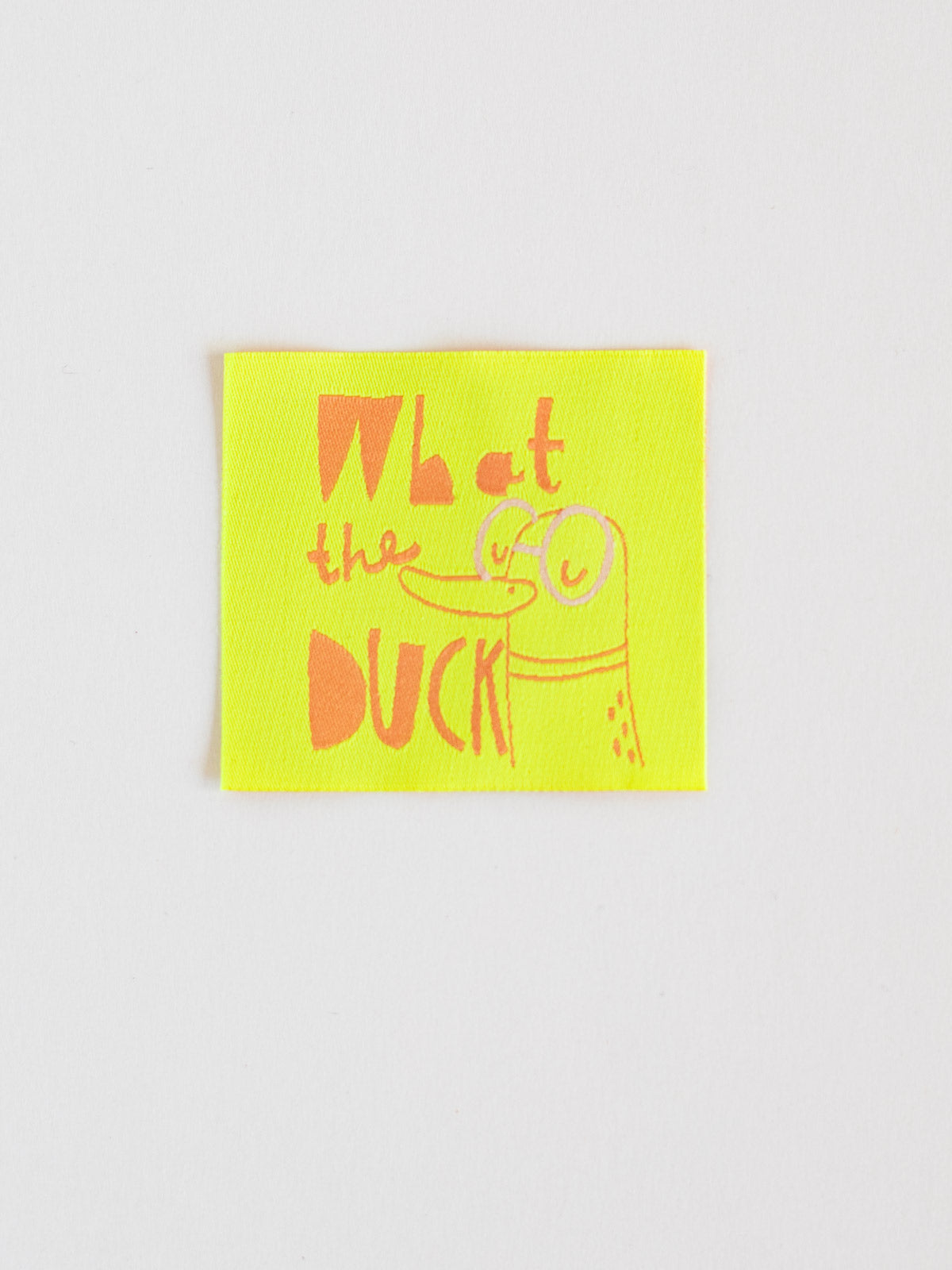 neongelbes Nähetiketten mit der aprikotfarbenen Aufschrift "what the duck" und Enten-Illustration von Halfbird