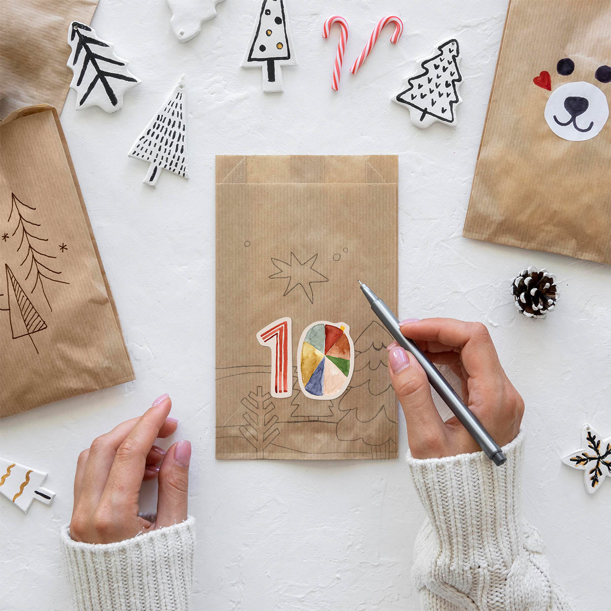 Frauenhände bemalen Butterbrottüten mit weihnachtlichen Motiven und nummerieren diese mit den Zahlenstickern von Halfbird