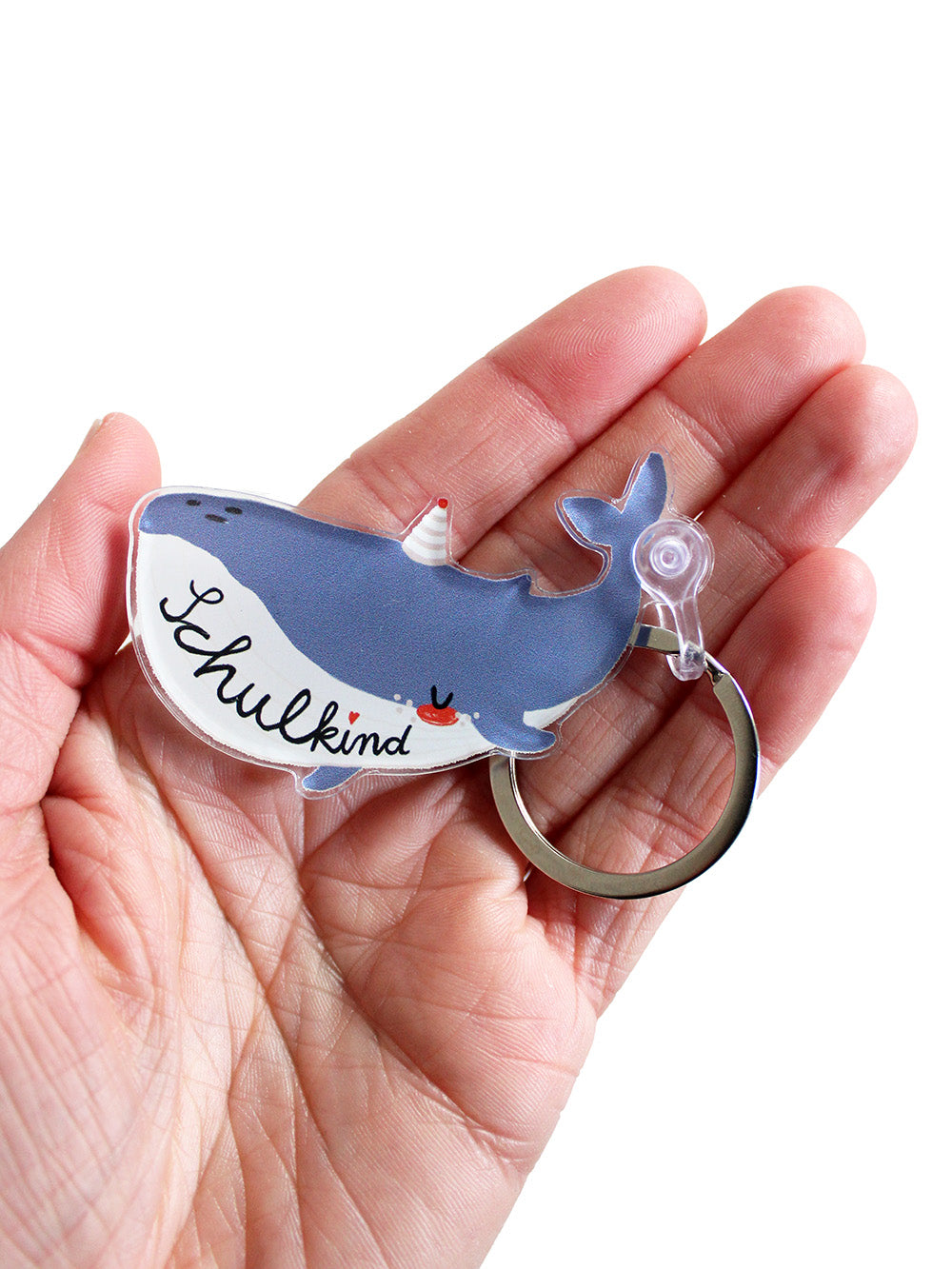 Nahaufnahme eines Schlüsselanhänger in Form eines Wals mit Schriftzug Schulkind in den Farben blau und weiß mit Partyhut in Hand liegend