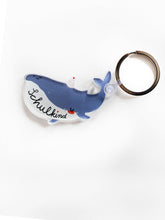 Ein Schlüsselanhänger mit Schlüsselring und Anhänger in Form eines Wals mit Schriftzug Schulkind in den Farben blau und weiß mit Partyhut