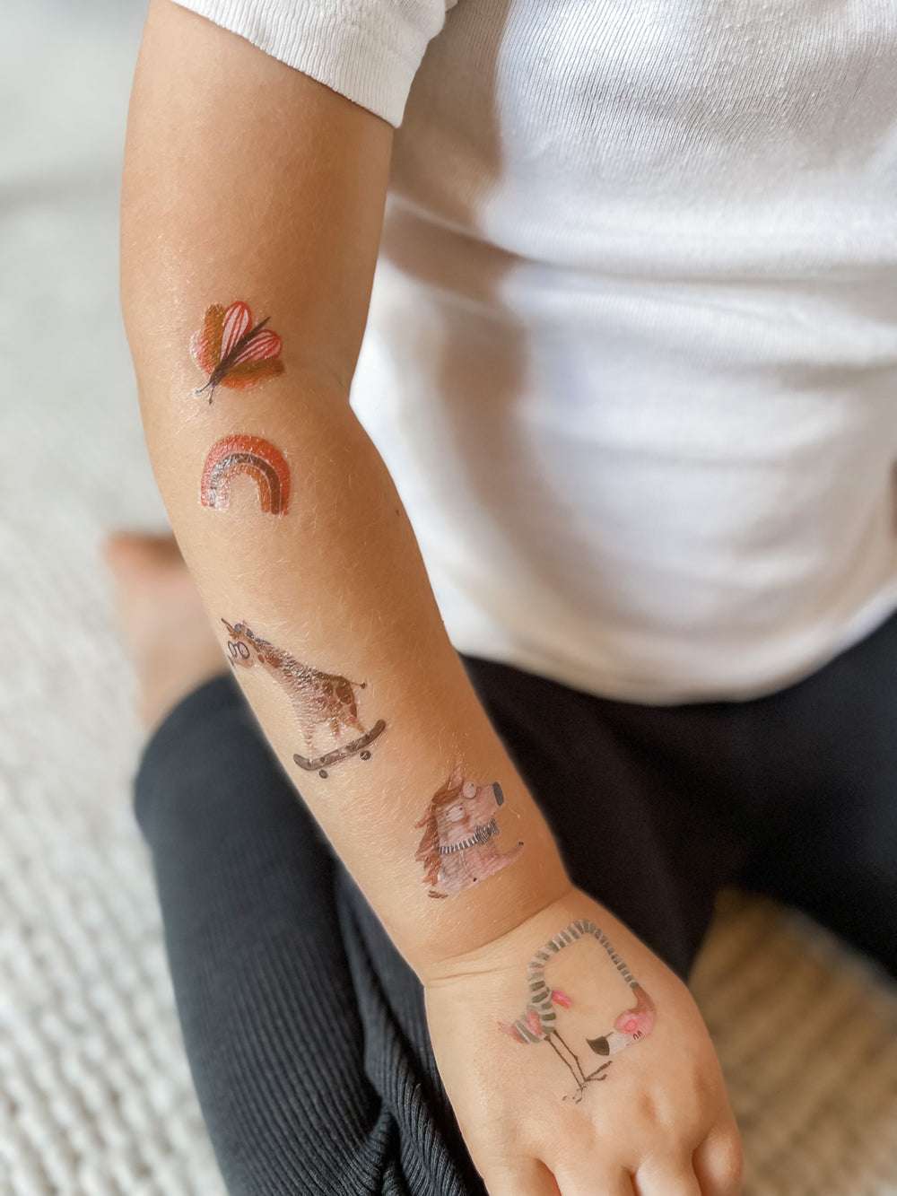 Kind hat einen tättowierten Arm mit Schmetterling, Regenbogen, Giraffe, Einhorn und Flamingo von halfbird