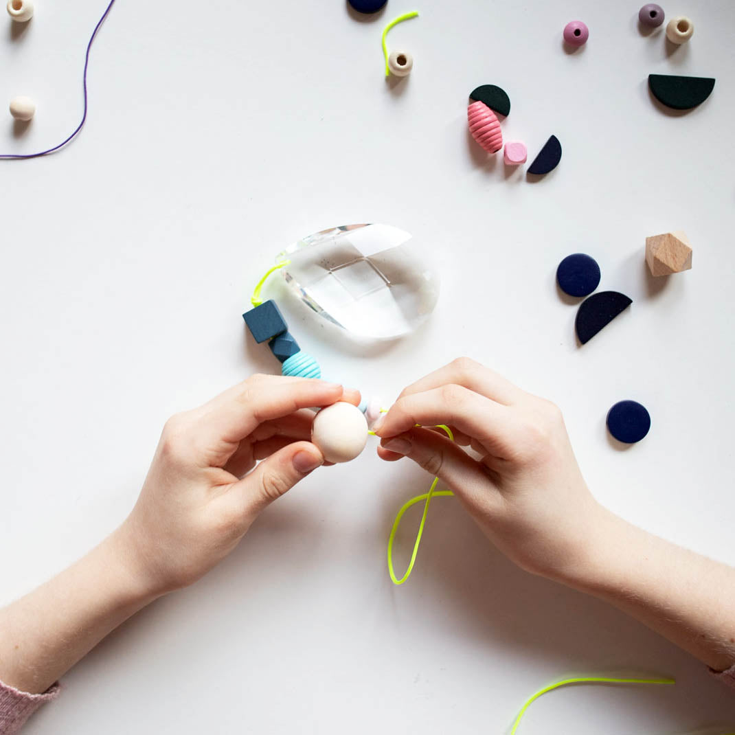 Hände fädeln Perlen auf eine neonfarbende Schnur auf