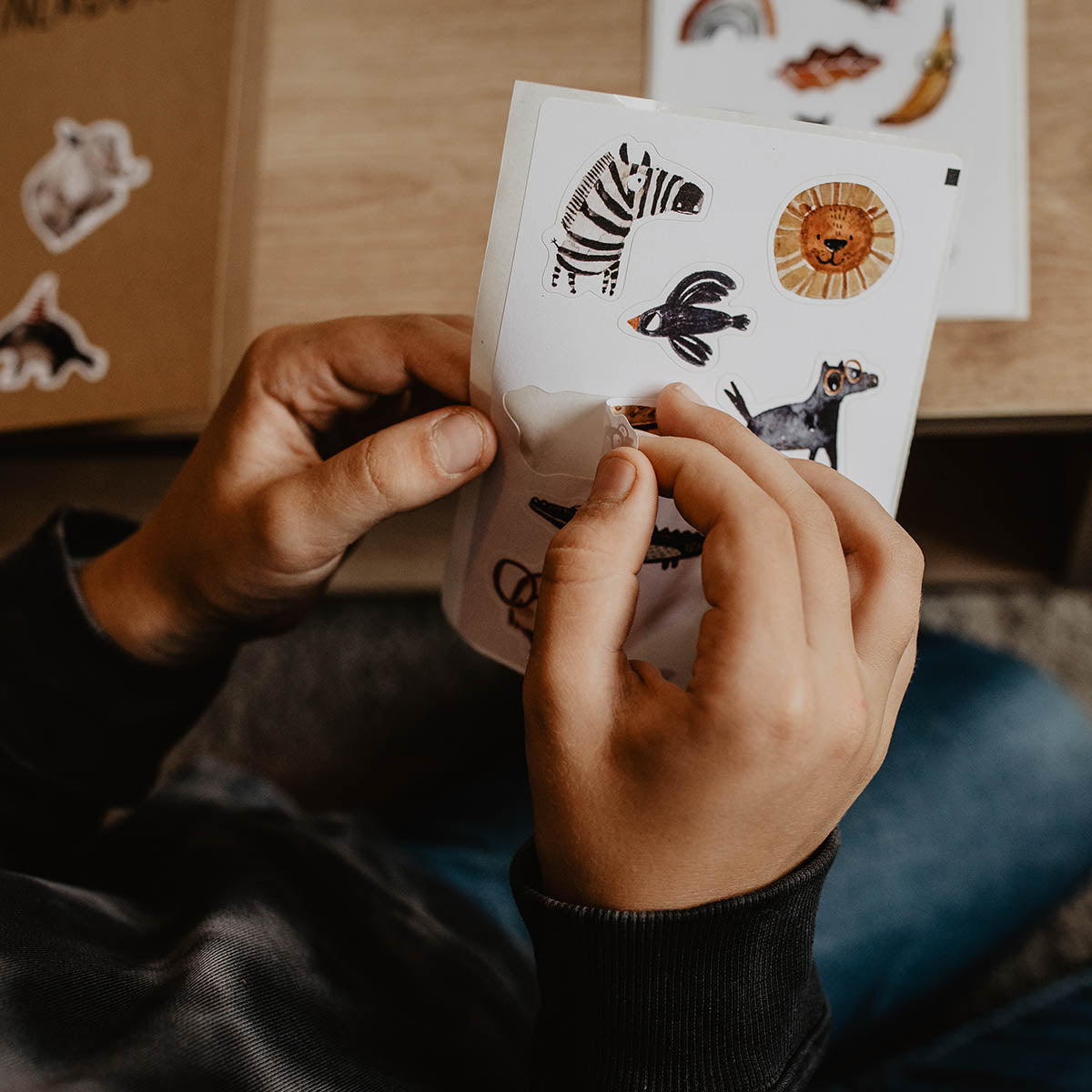 Kind zieht einen papiersticker vom Stickerbogen ab auf dem auch zebra, Vogel, Löwe, Pferd und Krokodil sind