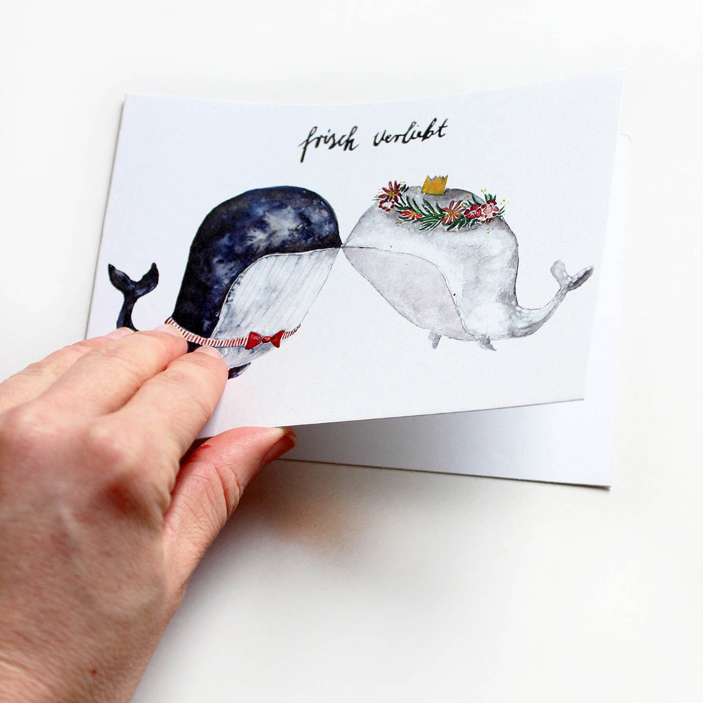 Hand klappt eine Klappkarte auf zur Hochzeit mit zwei sich küssenden Walen