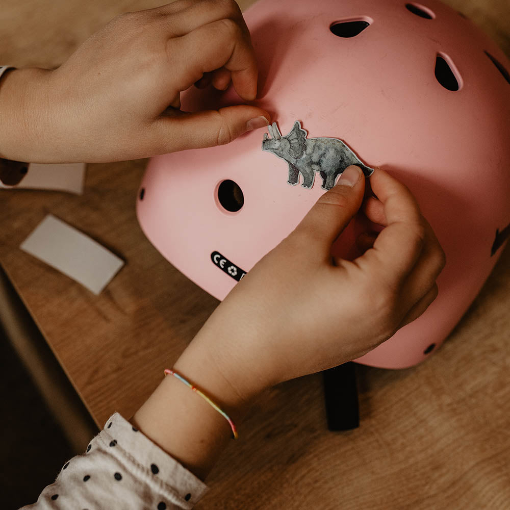 Kind klebt mit seinen Händen einen reflektierenden Aufkleber Dino auf seinen rosa Helm