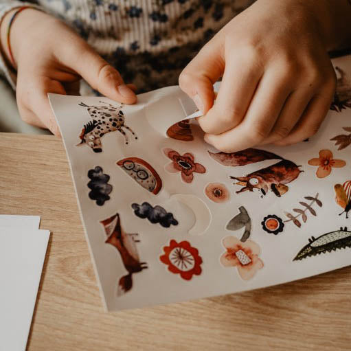 Kind nimmt einen Regenbogen Sticker vom Sticker Set mit Einhorn, Fuchs, Blumen, Eichhörnchen und schmetterling