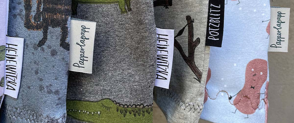 Stoffetiketten angenäht an kinderkleidung. Die Etiketten haben den SChriftzug heidewitzka, potzblitz und Papperlapapp