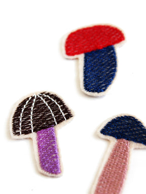 Detailansicht von drei gestickten Pilz Aufnäher in lila braun, rot blau und blau lachs