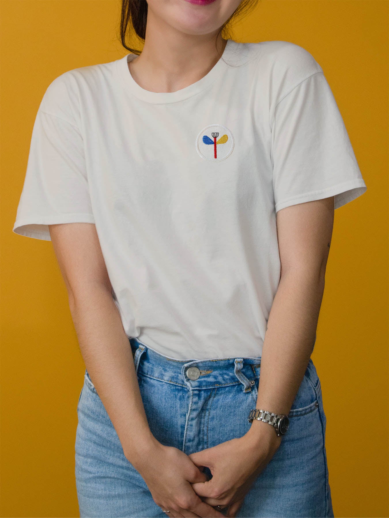 Frau mit weiße T-shirt und einem runden Patch auf der Brust mit einer peace blume in blau rot gelb