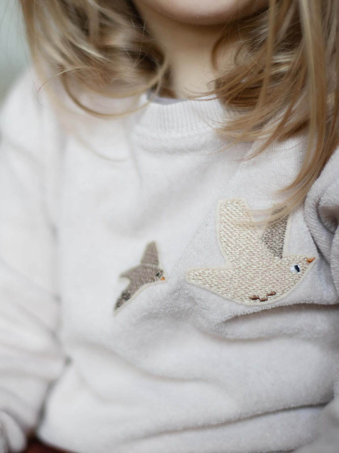 zwei Vogel Patches auf einem weißen Frottee Pulli von einem Kind