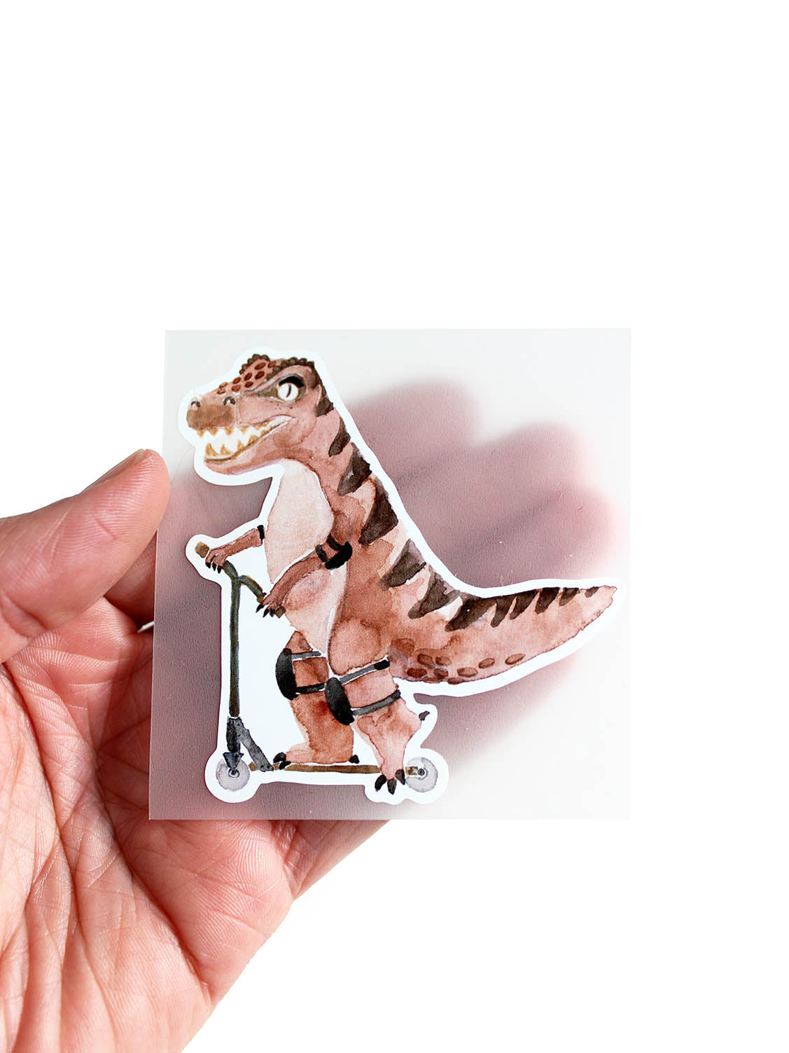 Hand hält ein Bügelbild mit einem roten T-rex auf einem Roller