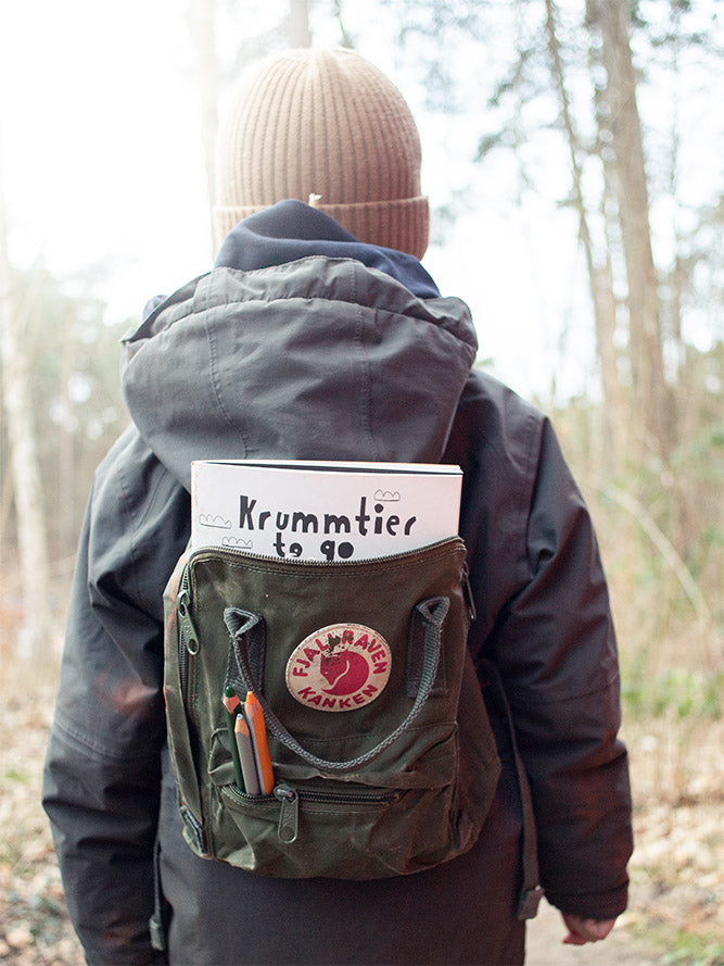 Kind mit Rucksack im Wald in dem rucksack steckt ein krummtier to go malbuch und stifte