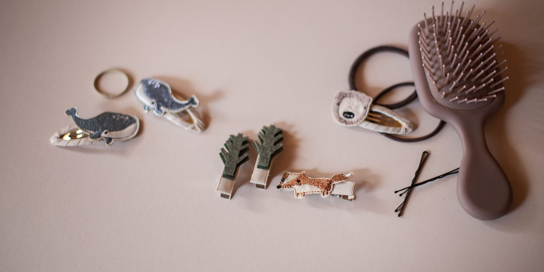 auf einem rosa tisch liegen haarspangen und clips mit wal, bäumen, Fuchs und Bär, daneben eine braune bürste und Zopfgummis