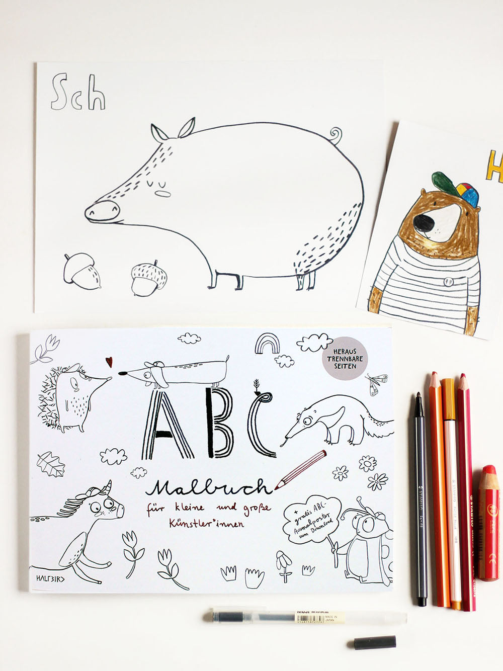 Flatlay Bild mit einem abc malbuch, stiften, einer karte ausgemalt mit einem bär und dem Wort Hi sowie den Buchstaben sch und einem schwein