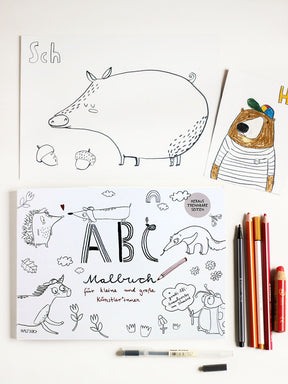 Flatlay Bild mit einem abc malbuch, stiften, einer karte ausgemalt mit einem bär und dem Wort Hi sowie den Buchstaben sch und einem schwein