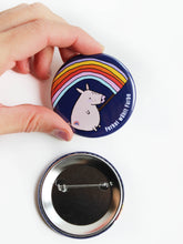 Ansteckbutton mit sicherheitsnadel in dunkelblau mit Schweinchen, dass eine bunte regenbogenfahe hält und ein Regenbogen auf dem Po hat seitlich steht der Text Ferkel wählt Farbe