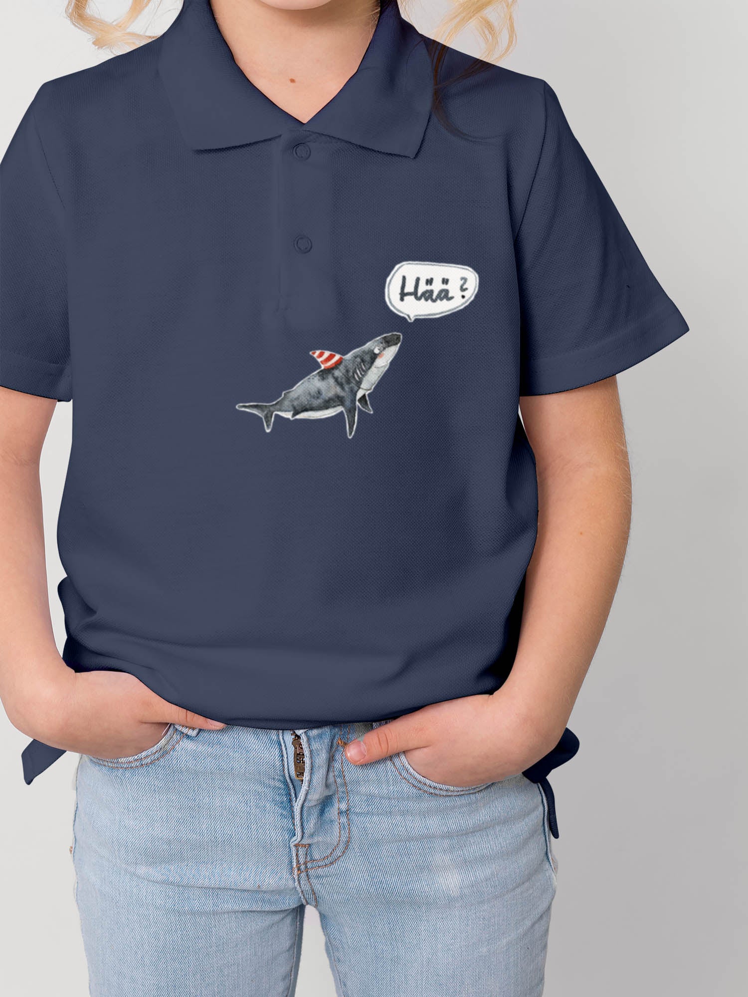 Kind trägt ein polo shirt in blau und darauf ist ein hai und ein Hää bügelbild von halfbird gebügelt