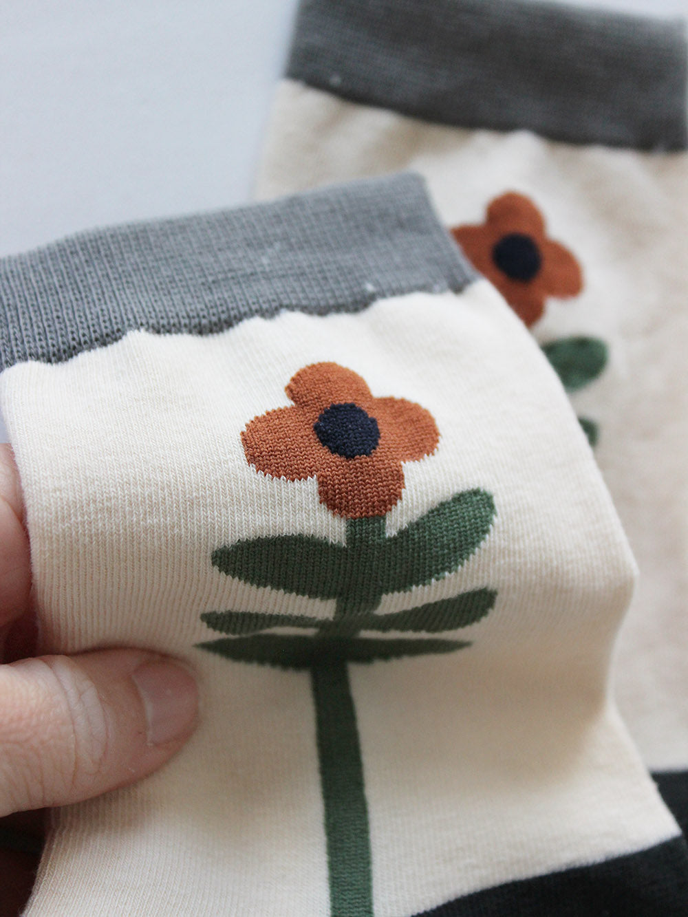 Nahansicht  von weißen Socken mit einer grün-orangenen Blume, die den Fuß entlang rankt und grauem Bündchen