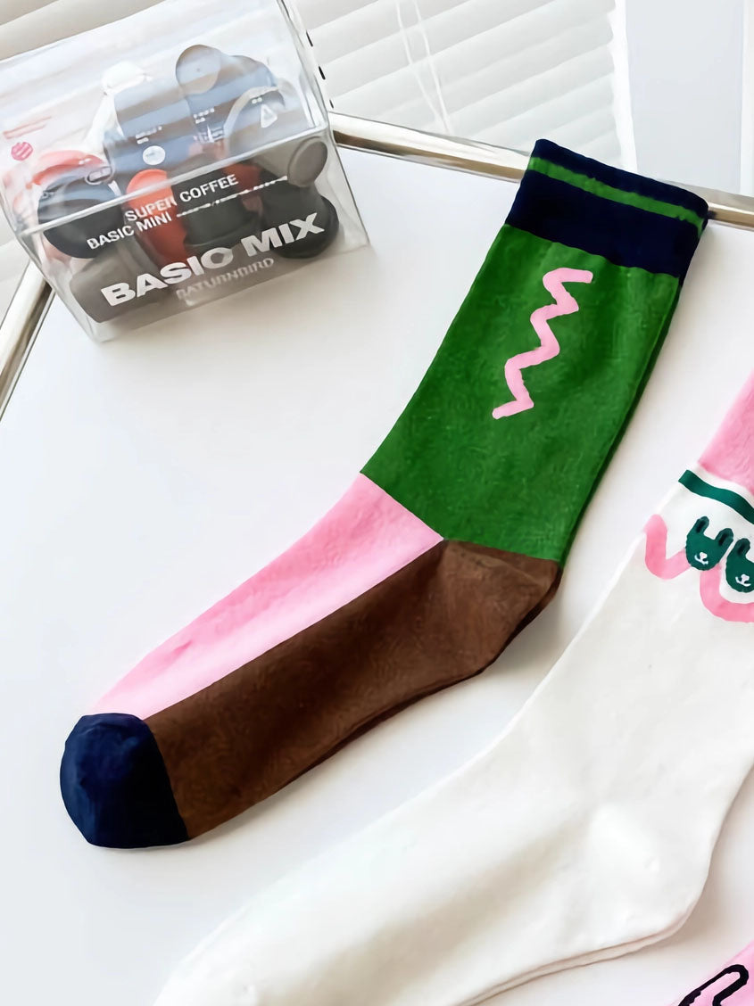 Flatlay Bild von Color Blocking Socken in braun, grün und pink sowie einem geometrischen Muster in der grünen Fläche unterhalb des Bundes