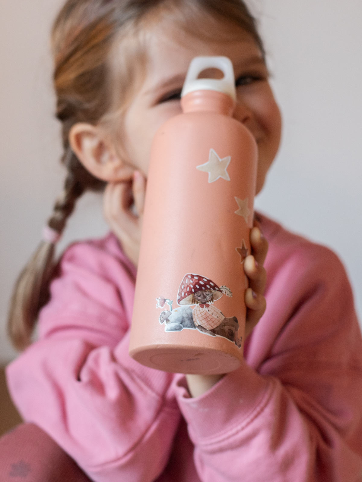Kind hält eine rosa Metallflasche hoch mit feen stickern darauf und sternen