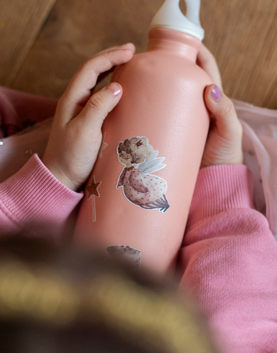 Kind hält eine apricot rosa farbene Trinkflasche aus Metall im Schoß und darauf ist ein feen sticker und STernen und feenstaub und ein Einhorn von halfbird