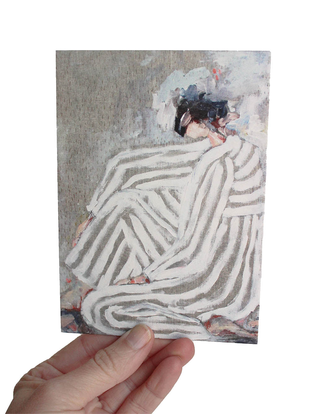 Hand hält eine Postkarte hoch, auf der eine sitzende Frau gemalt ist in gestreifter kleidung