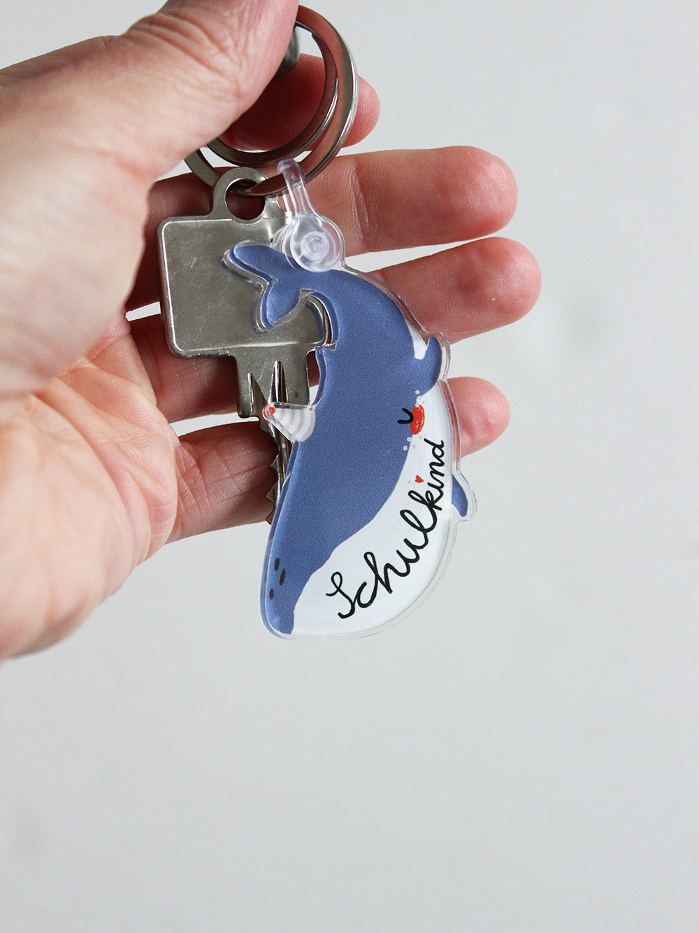Nahaufnahme eine Schlüssels in Hand liegend mit einem Schlüsselanhänger in Form eines Wals mit Schriftzug Schulkind in den Farben blau und weiß mit Partyhut