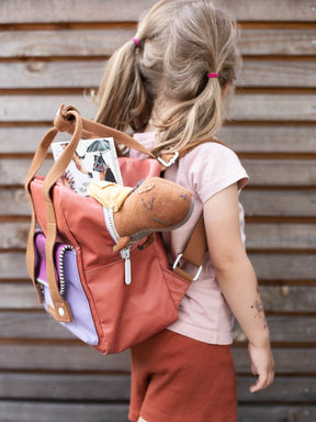 Kind trägt einen Rucksack und darin steckt ein selbstgenähter Dino und ein Freundebuch von halfbird