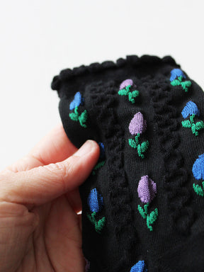 Detailansicht von schwarzen, schlichten Socken mit blau- und rosafarbenen Tulpenblüten mit Strickstruktur