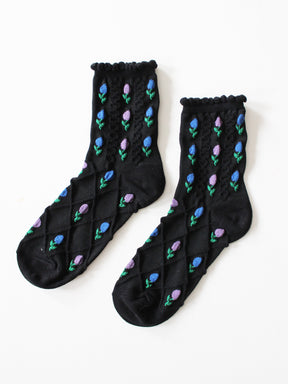 Flatlay schwarze, schlichte Socken mit blau- und rosafarbenen Tulpenblüten mit Strickstruktur