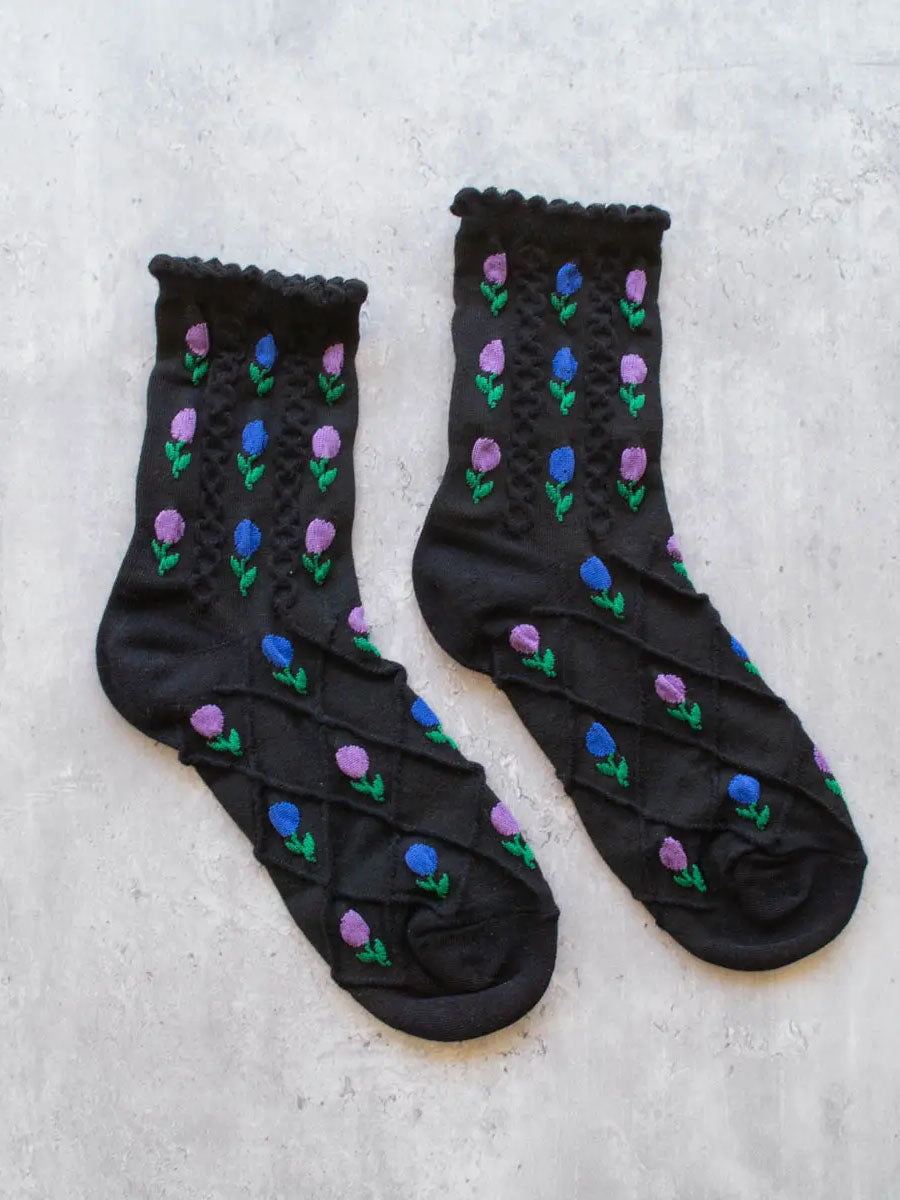 Flatlay von schwarzen, schlichten Socken mit blau- und rosafarbenen Tulpenblüten mit Strickstruktur