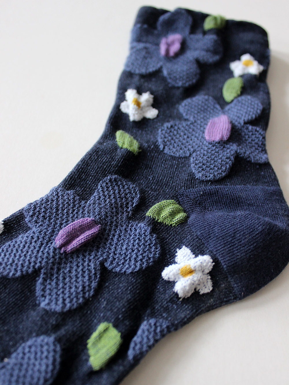 Detailansicht von dunkelblauen Socken mit erhabener Struktur mit großen taubenblauen und weißen Blumen