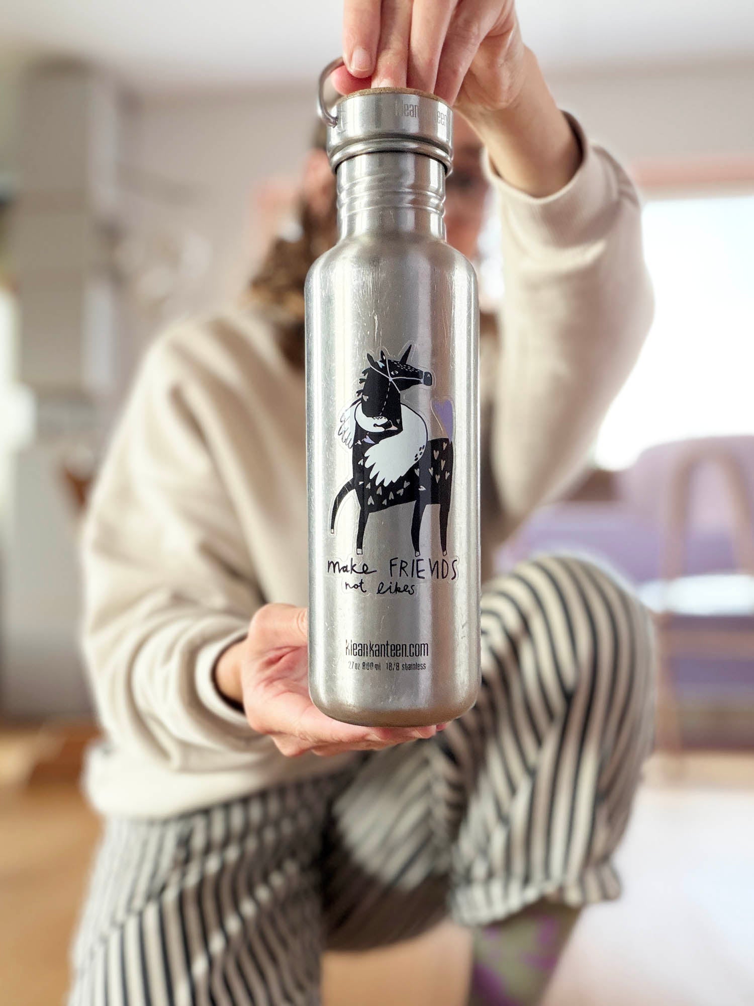 Mona hält Edelstahlflasche mit transparentem Vinylsticker Make Friends not Likes mit Pferd- und Schwanmotiv von Halfbird