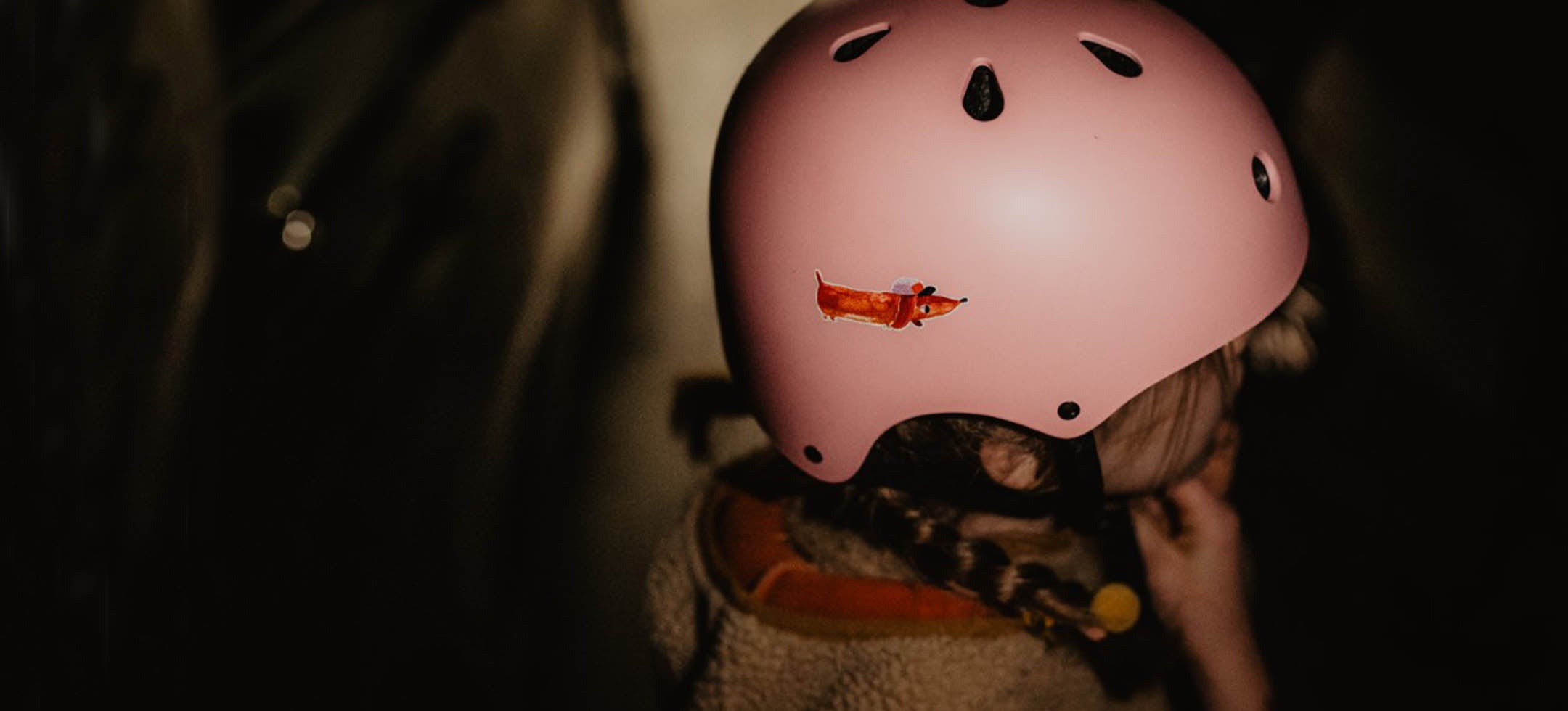 Kind zieht sich bei dunkelheit seinen rosa helm auf den kopf, darauf klebt ein reflektierender sticker dackel von halfbird