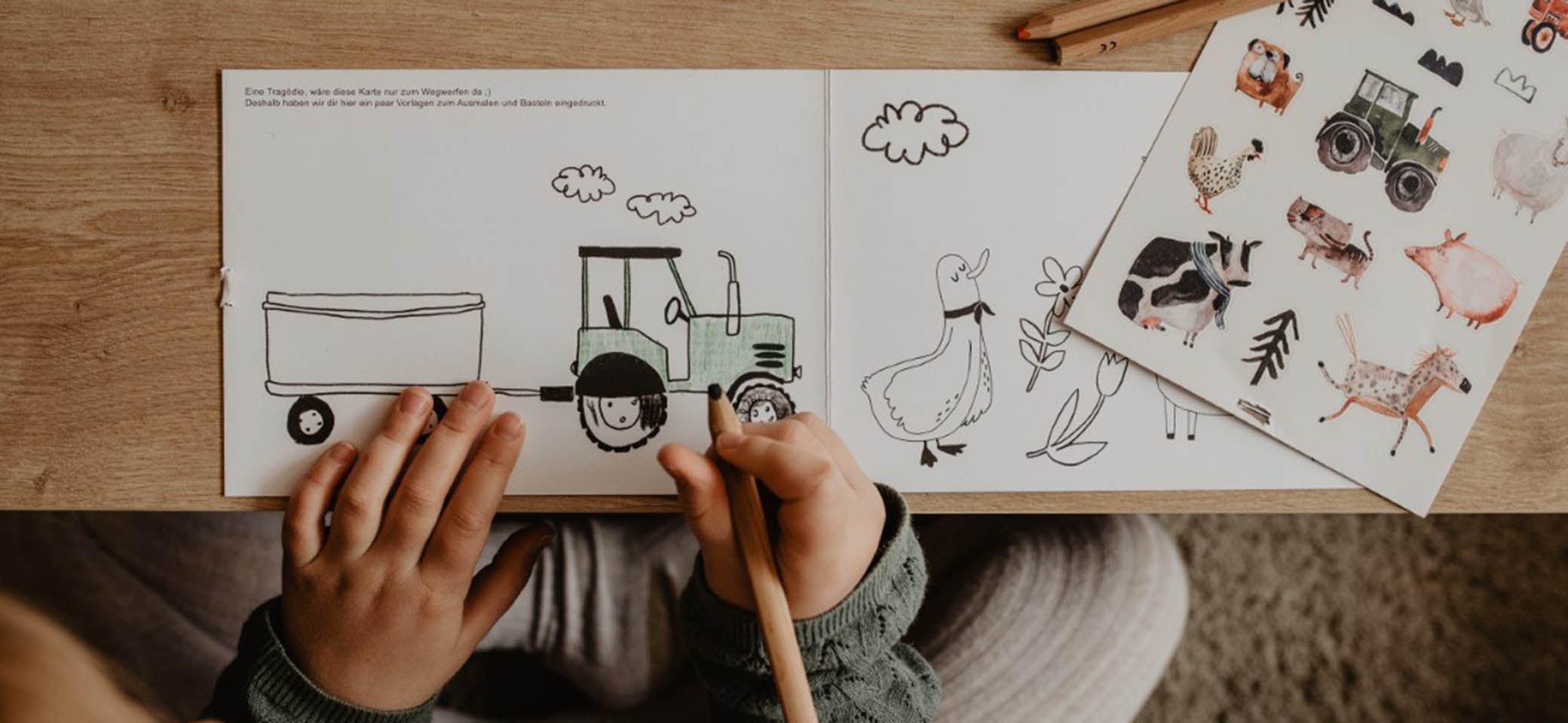 Kind malt einen Traktor aus mit buntstiften, daneben liegen auf dem tisch bauernhof sticker für die spülmaschine mit kuh, schwein, pferd, traktor, hund huhn etc.