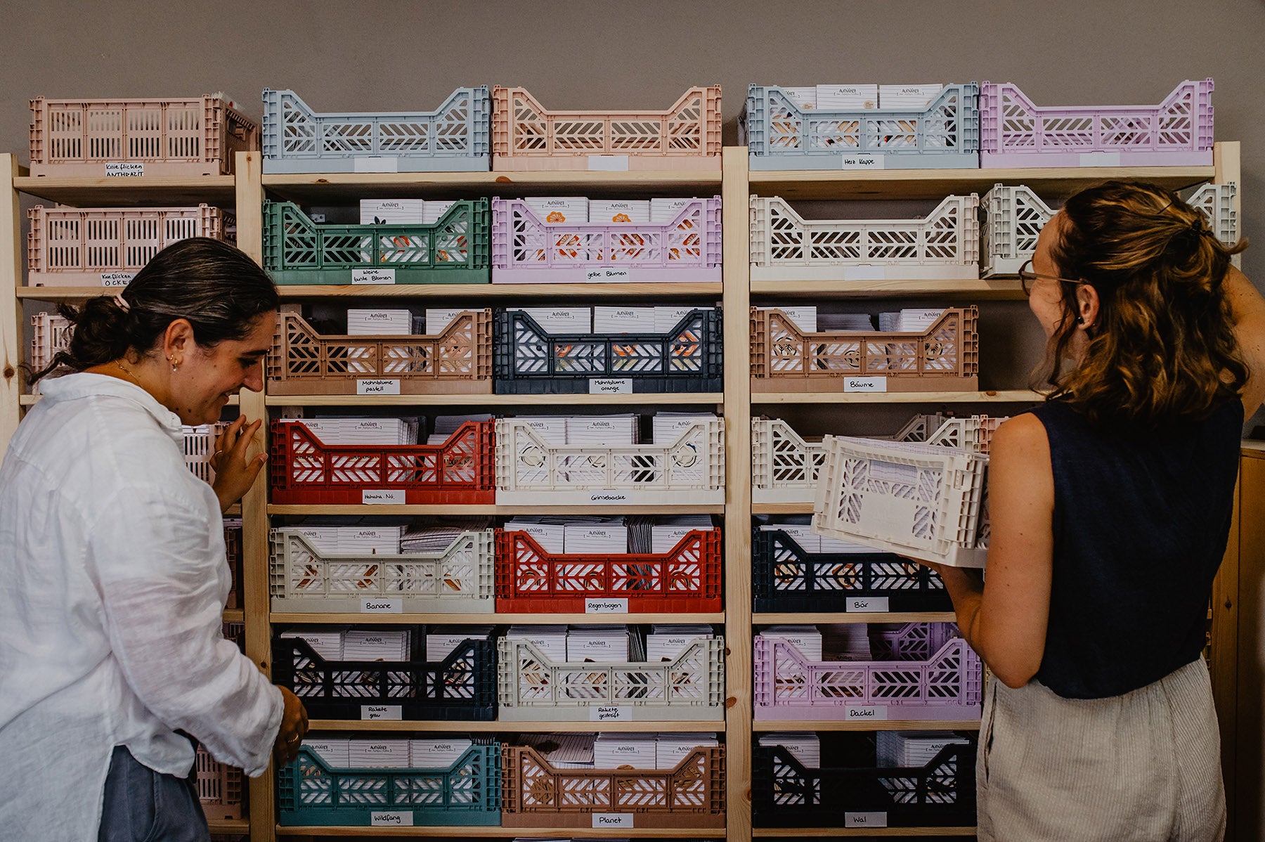 zwei Frauen stehen vor einem Regel voller bunter Kisten im Atelier halfbird und sortieren diese ein