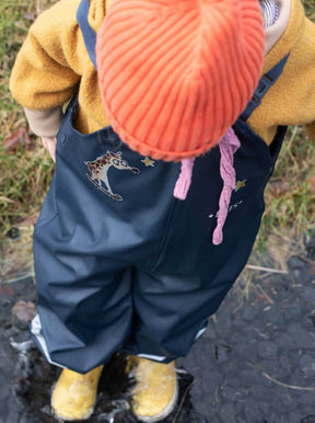 Kind steht mit seiner Matschhose in einer pfüte und hat auf der Hose reflektierende bügelbidler aufgebügelt von halfbird. eine giraffe unn sterne