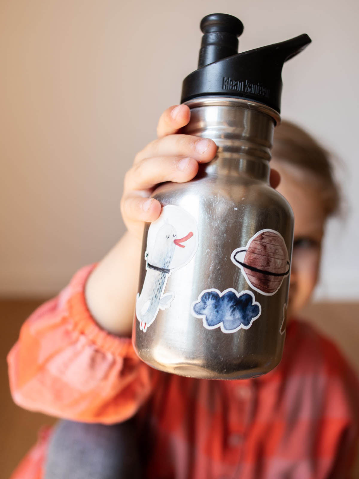 Kind hält eine metallflasche von klean kanteen hoch auf der Spülmaschinenfeste Aufkleber Planet, wolke und gans im weltall kleben