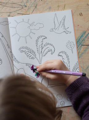 Kind malt eine Seite im Krummtier to go Malbuch mit Filzstiften aus auf denen Dinos zu sehen sind