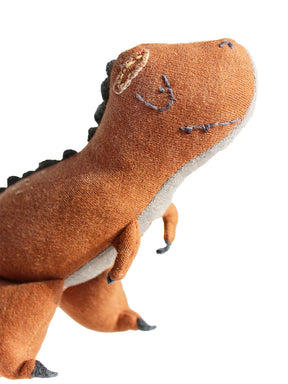 Nahansicht eines Dino Kuscheltieres mit gestickten Augen und einem Mund in rostrot