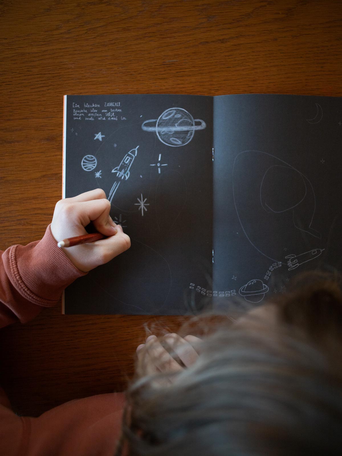 Kind malt mit weißem Stift auf schwarzen seiten in einem Malbuch
